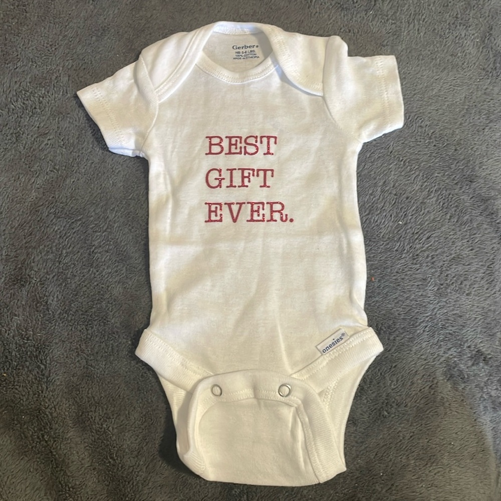 White Newborn Onesie with the saying “BEST GIFT EVER”.